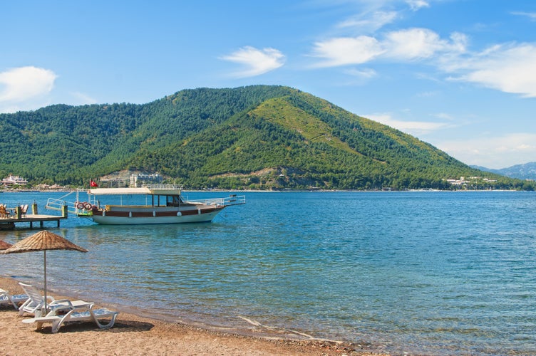 Photo of tourist boat moored at small pier at Icmeler beach with green hills at background in Aegean sea, Marmaris, Turkey.