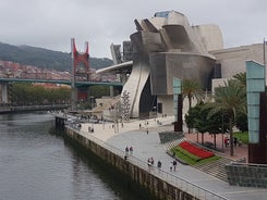 Photo of aerial view of Bilbao, Spain city downtown with a Nevion River, Zubizuri Bridge and promenade. Mountain at the background, with clear blue sky.