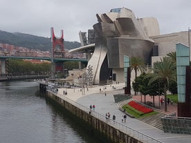 Photo of aerial view of Bilbao, Spain city downtown with a Nevion River, Zubizuri Bridge and promenade. Mountain at the background, with clear blue sky.