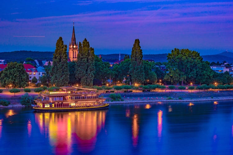 photo  of view of Skyline of Bonn, Germany. Beautiful night shot of great german city. Panorama with boat, trees, and historic architecture reflected in the water.