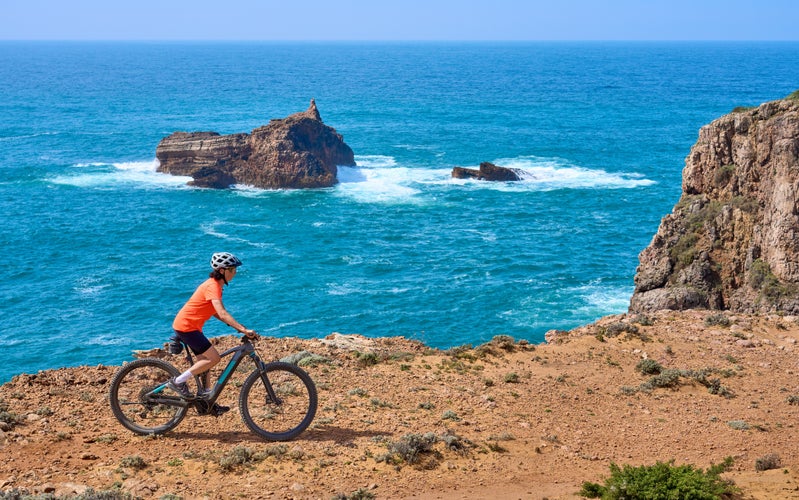 happy active senior woman cycling on the the rocky cliffs of the Vicentina coast of  Portugal near Sagres and Vila do Bispo 