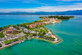 Photo of Old harbour Porto Vecchio with motor boats on turquoise water, green trees and traditional buildings in historical centre of Desenzano del Garda town, Northern Italy.