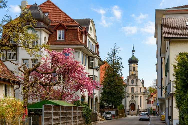 photo of view of A picturesque street in the city of St. Gallen with houses in traditional Swiss style among flowering trees, an ancient church in the background