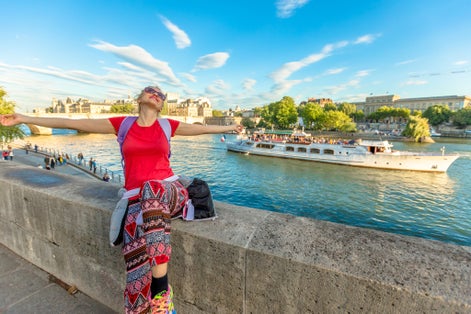 photo of Caucasian lifestyle woman with open arms enjoying the Seine and Pont Neuf on a blurred background in Paris, France.