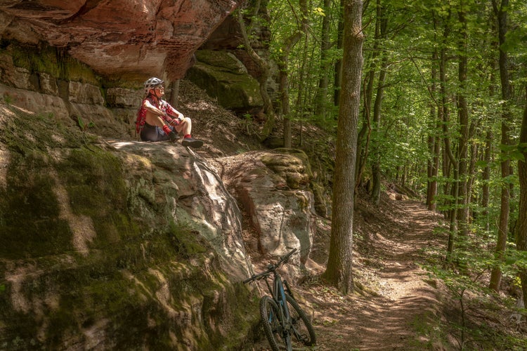 nice and active senior woman riding her electric mountain bike on a rocks trail in the Pfaelzerwald forest near the city of Pirmasens in Rheinland-Pfalz, Germany