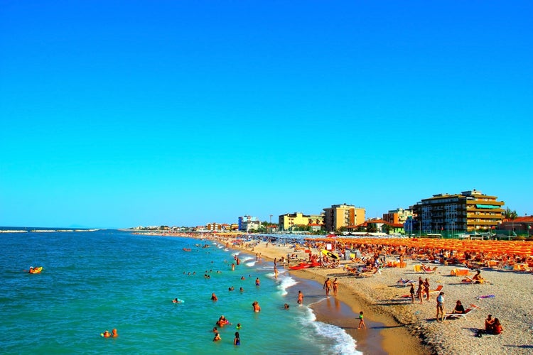 Interesting shot of crowded beach resorts in Fano with pure azure sea washing the sandy shores, colored parasols and buildings in the background on a fine summer day