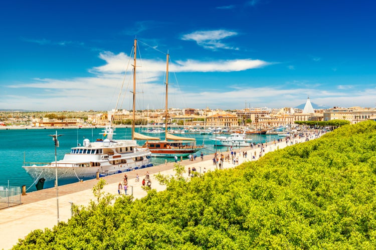 Beautiful view of the harbor in Syracuse with people walking along the promenade. Cityscape of Ortygia Island, Sicily, Italy