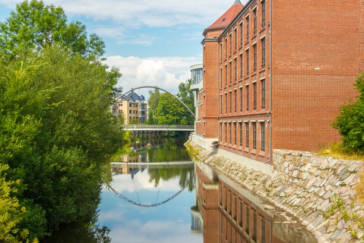 Photo of View on the calm river with reflection in Chemnitz, Germany. Former industrial building on the one bank and a small bridge over the river. Concept of new and old.