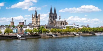 Cologne Aerial view with trains move on a bridge over the Rhine River on which cargo barges and passenger ships ply. Majestic Cologne Cathedral in the background.