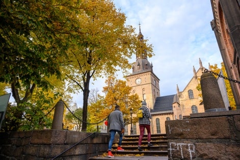 Two people are walking up the stairs to the Oslo Cathedral, located in the center of Oslo, Norway. In autumn, the leaves turn yellow and orange.