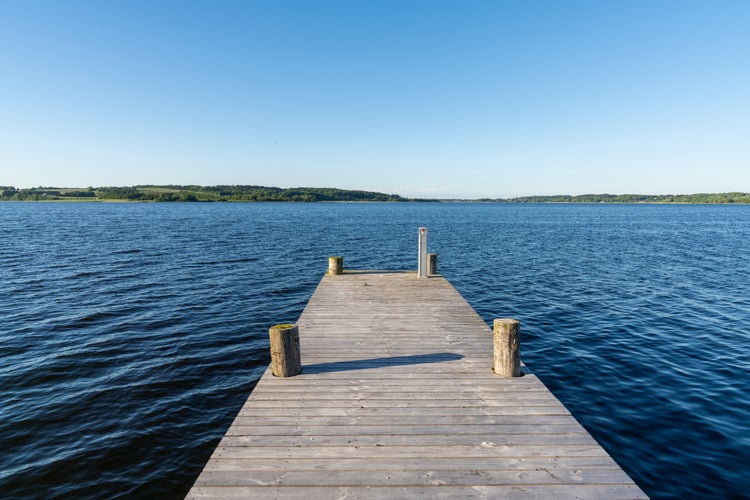 photo of view of A wooden boardwalk leading out into the dark blue waters of a fjord under a cloudless blue sky