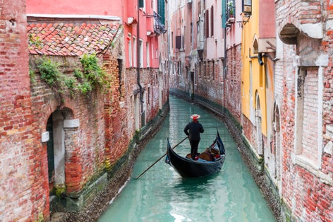Venetian gondolier punting gondola through green canal waters of Venice, Italy.