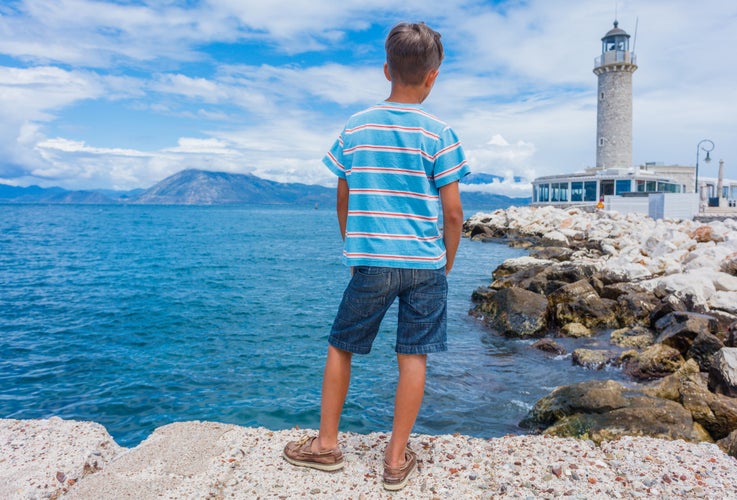 Back view of cute boy looking at the Patras lighthouse, Peloponnese, Greece. The lighthouse located on the seafront near Saint Andrew's Cathedral, is the symbol of Patras Town.