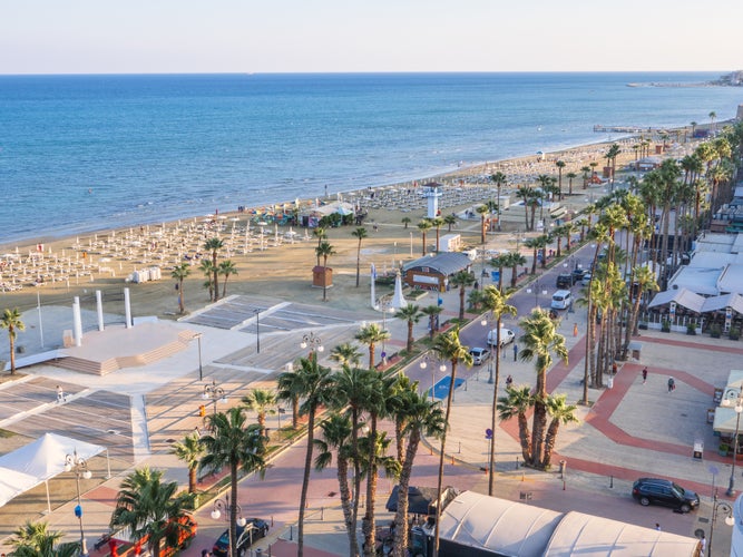 Photo of top aerial view overlooking Finikoudes Palm tree promenade, road with cars and central beach near the Mediterranean sea in Larnaca city, Cyprus.