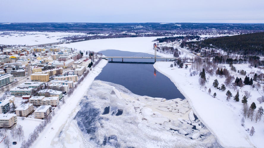 Photo of beautiful winter landscape with buildings and a bridge over Ounasjoki River in Rovaniemi, Finland.