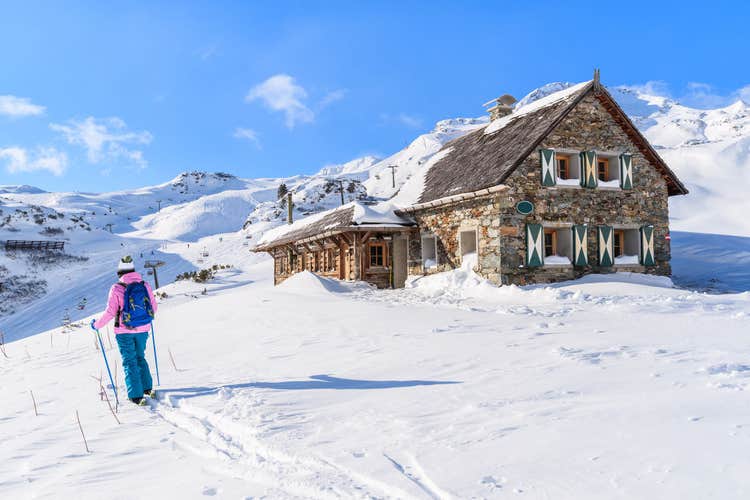 photo of young woman skier walking past mountain hut in Obertauern winter resort, Austria.