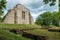 photo of remaining wall of Riseberga Abbey located at Riseberga in Sweden. With dark sky green trees and sunshine that illuminates the stone wall.