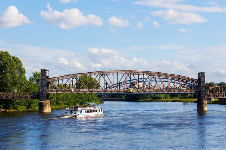 Tourist boat cruises under old historic iron bridge on Elbe River in Magdeburg, Germany with blue sky clouds background landscape. Saxony-Anhalt center cityscape sightseeing water trip