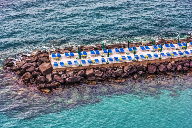 Photo of beach chairs and umbrella on a breakwater in Sorrento, Italy.