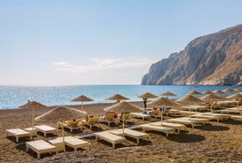 Photo of aerial view of black Perissa beach with beautiful turquoise water, sea waves and straw umbrellas, Greece.