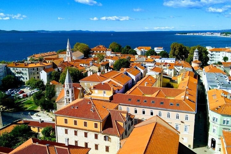 Aerial view of Zadar_s old town with orange rooftops, church spires, lush greenery, and the Adriatic Sea under a bright blue sky..jpg