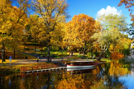 City park of the city of Riga with a canal with bright autumn leaves against the blue sky and reflections in the water