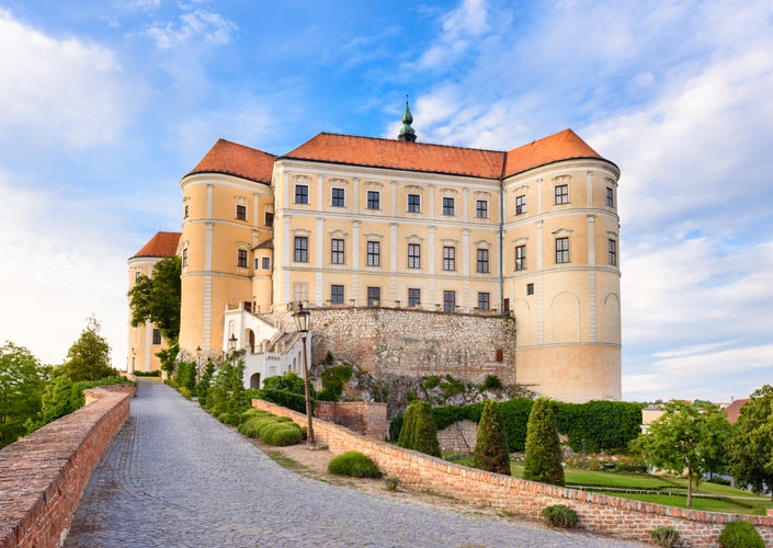 Photo of Mikulov castle or Mikulov Chateau on top of rock. View from garden of castle with beautiful staircase and bright blue sky with clouds in background, Moravia, Czech Republic.