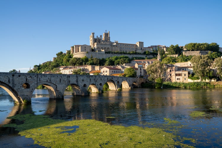 Gothic Cathedral on top of a hill in a town with a river and a stone bridge to cross it. Narbonne France