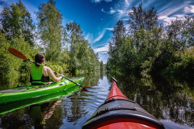 Middle-aged Caucasian Scandinavian women kayaking in small river Savaron in forest.