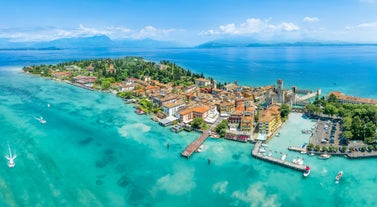 Photo of Old harbour Porto Vecchio with motor boats on turquoise water, green trees and traditional buildings in historical centre of Desenzano del Garda town, Northern Italy.