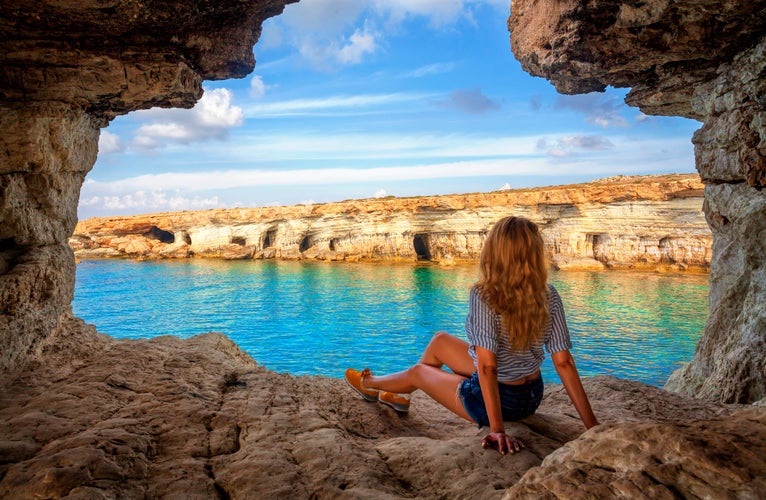 View from sea cave near Cape Greko(Capo Greco) of Ayia Napa and Protaras on Cyprus, Mediterranean Sea. Attractive woman enjoys the sea air on seaside. Holidays at Ayia Napa Resort, Cyprus