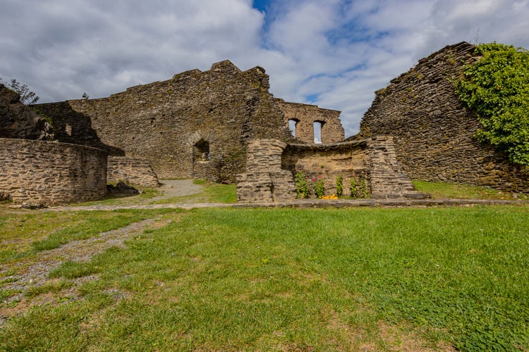 Photo of Outdoor ruins of the medieval castle of Bourscheid, outer esplanade with weathered stone walls in the background, sunny day with a blue sky with white clouds in Luxembourg.