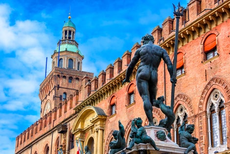 photo of The Fountain of Neptune (Fontana di Nettuno) with Palazzo d'Accursio in background in Bologna, Italy. Architecture and landmark of Bologna. Cityscape of Bologna.