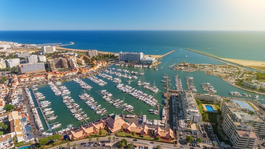 Photo of aerial view of the bay with yachts and sandy beach in Vilamoura, Loule, Algarve, Portugal on a sunny day.