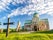 Photo of colorful morning shot of the famous Bagrati Cathedral in Kutaisi, Georgia, with beautiful clouds over blue sky, green grass and a large Christian cross in front of the building.