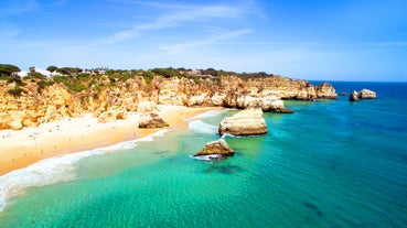 Photo of beautiful aerial view of the sandy beach surrounded by typical white houses in a sunny spring day, Carvoeiro, Lagoa, Algarve, Portugal.