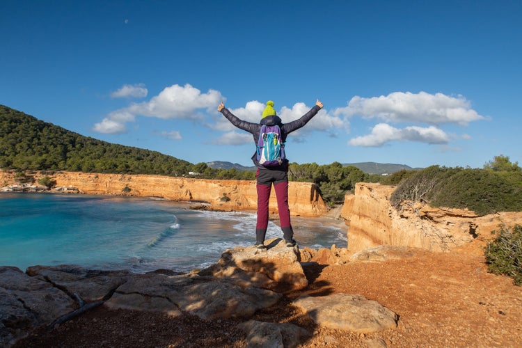 Tourist with a backpack standing on the edge of the clay cliff of Sa Caleta bay. Ibiza. Spain.jpg