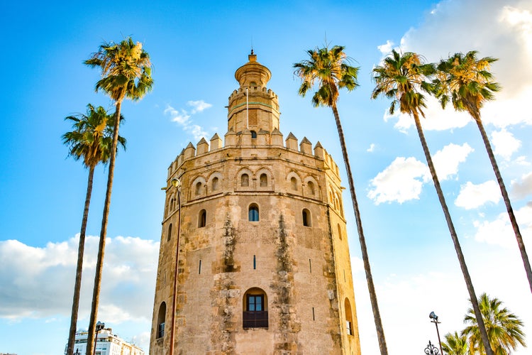 Photo of Torre del oro, historical limestone tower of gold under blue sky and palm tree in Seville, Spain.