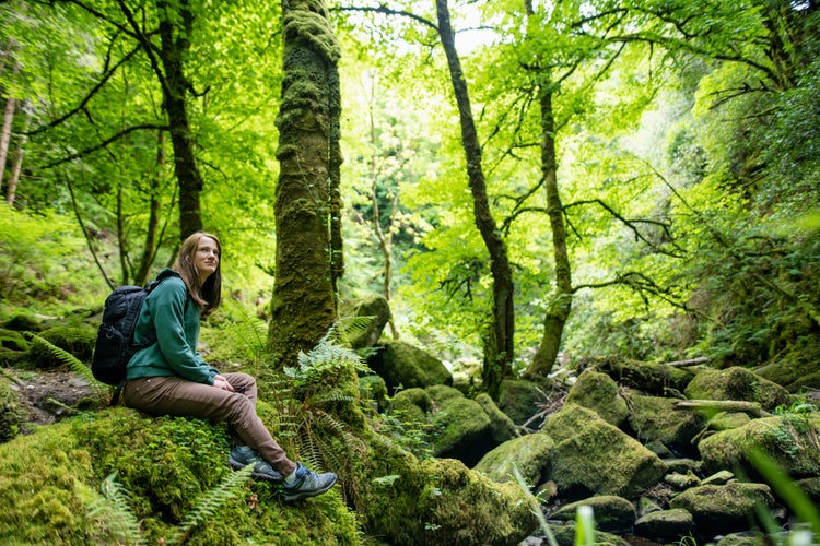 Tourist admiring small waterfalls near Torc Waterfall, one of most popular tourist attractions in Ireland, located in woodland of Killarney National Park. Ring of Kerry tourist route, Ireland.