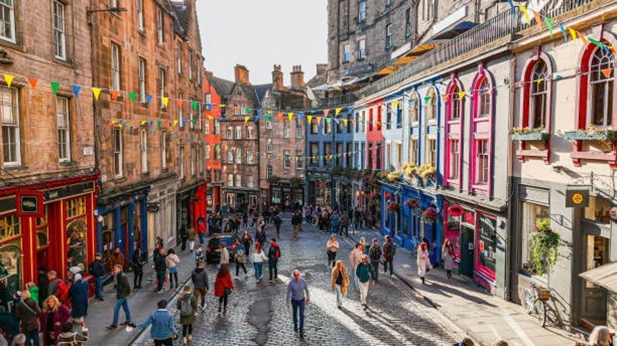 An aerial perspective of Victoria Street in Edinburgh, showcasing its vibrant, curved row of colorful buildings decorated with lively festival streamers.jpg