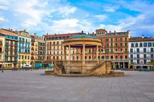 Photo of aerial view of Bilbao, Spain city downtown with a Nevion River, Zubizuri Bridge and promenade. Mountain at the background, with clear blue sky.