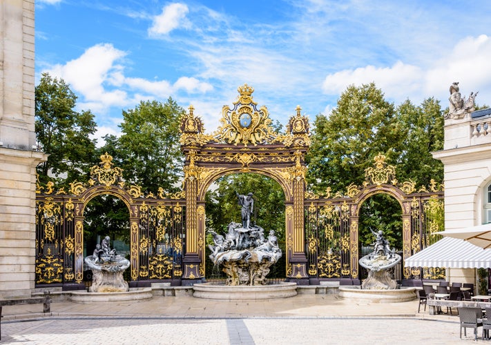 Photo of the fountain of Neptune in the Rococo style and the gilded wrought iron portico in the north-west corner of the Stanislas square in Nancy, France.