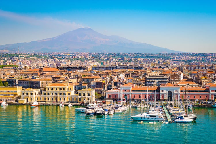 Catania-s harbor with yachts, historic buildings, and Mount Etna in the background under a blue sky..jpg