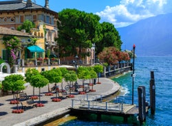 Photo of Old harbour Porto Vecchio with motor boats on turquoise water, green trees and traditional buildings in historical centre of Desenzano del Garda town, Northern Italy.