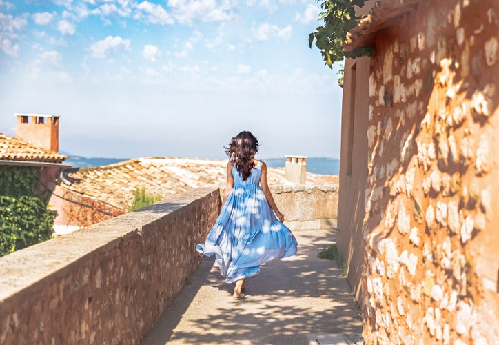 France, Provence medieval town Roussillon. Pretty young woman in blue dress walking down the street in Provencal old city. Travel and wanderlust concept. June - time of blooming lavender in Provence