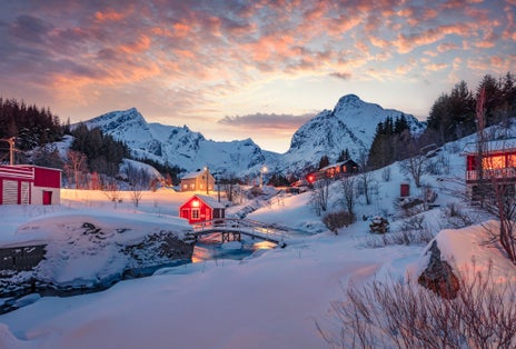 Snowy winter cityscape of Nusfjord town. Unbelievablesunset in Norway, Europe. Amazing evening view of Lofoten Islands with red wooden houses and small river. Life over polar circle.