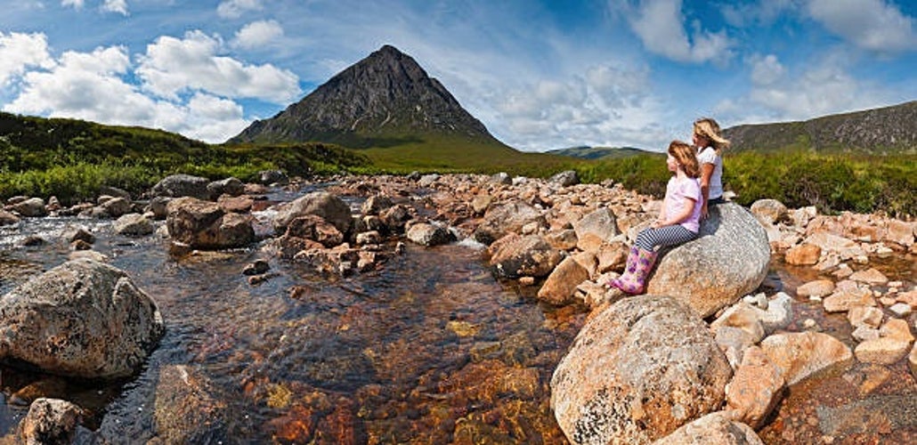 Two young children sitting on a rock beside a crystal-clear mountain stream, gazing at the iconic pyramid-shaped Buachaille Etive Mor in Glen Coe.jpg