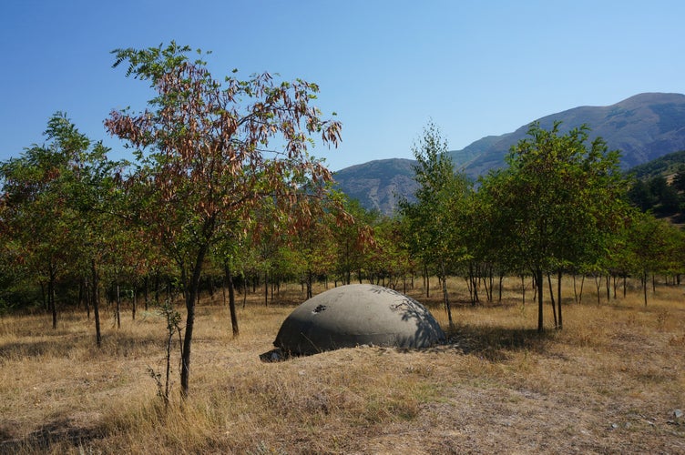 photo of view of Korçë, Albania - August 30 2015: Old communist bunker in a young grove with mountains in the background, Korçë, Albania.