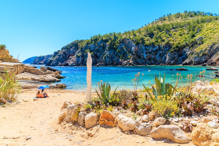 Couple of unidentified people sunbathing on secluded Cala d'en Serra beach, Ibiza island, Spain