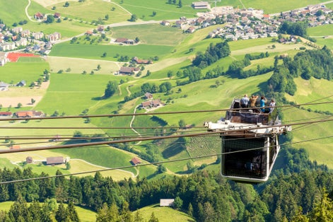 photo of tourists (faces not visible) climbing the cable car in an open car up Mount Stanserhorn in Switzerland and admire the magnificent aerial panorama of central Switzerland, mountains, villages and forest.